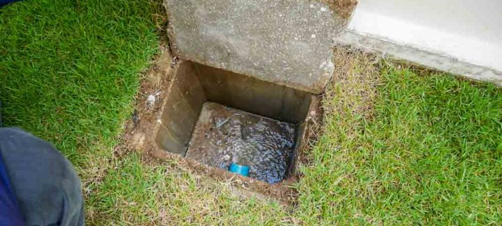 In the image, a worker's hand is seen lifting the sewer cover of a newly constructed house. This action symbolizes the final step in ensuring the plumbing infrastructure is connected and functional.